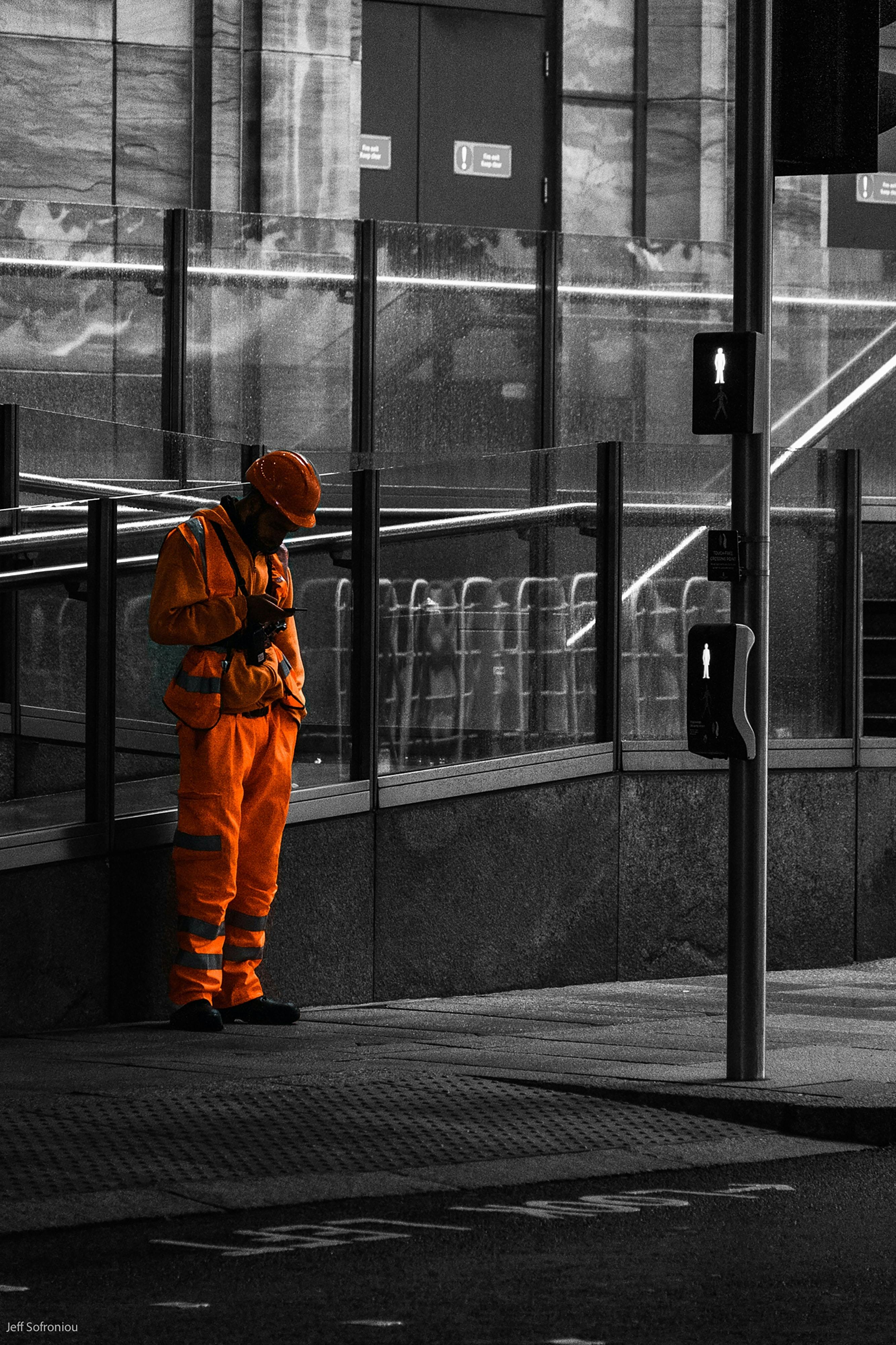 Male worker in full protective clothing stands by the side of a road looking at his phone